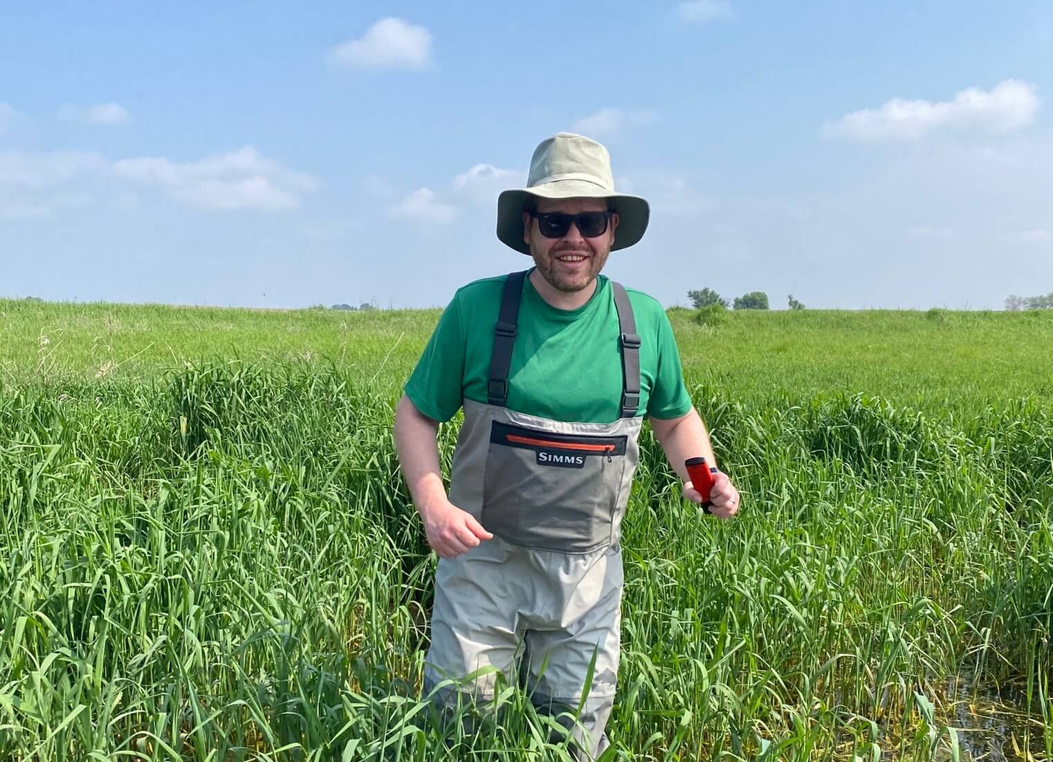 Researcher Charlie Loewen in a study wetland in Iowa holding a pH meter.